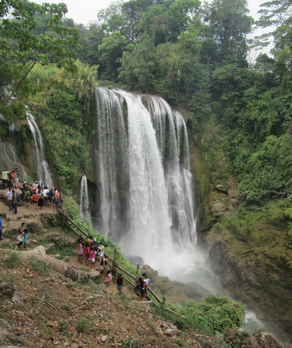 Pulhapanzak Waterfall cascading over a wide rock face into a misty plunge pool surrounded by tropical vegetation