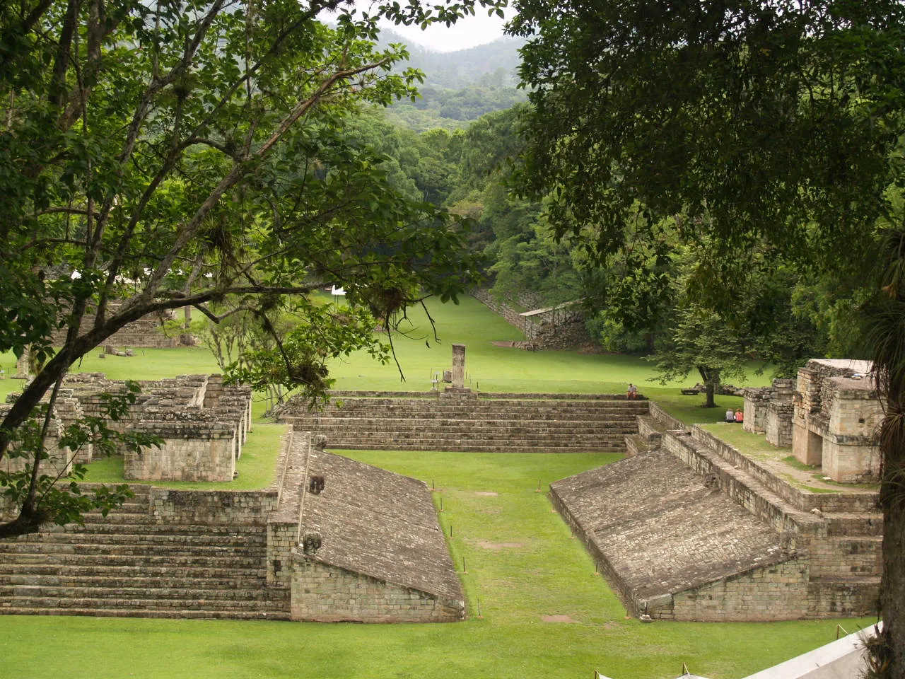 The Maya ballcourt at Copán seen from above, with sloped stone walls flanking the playing alley and forest beyond