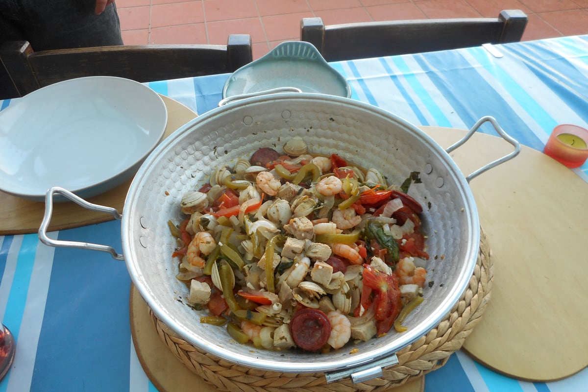 A cataplana copper pot dish open at the table, filled with clams, prawns and chorizo